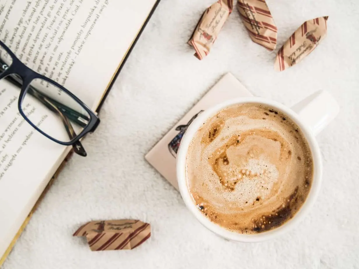 فنجان القهوة الصباحية بجانب كتاب ونظارات.