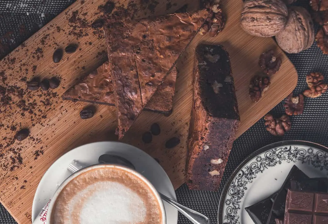 فنجان قهوة وشريحة من كعكة الشوكولاتة على لوح تقطيع خشبي في مقهى مريح.