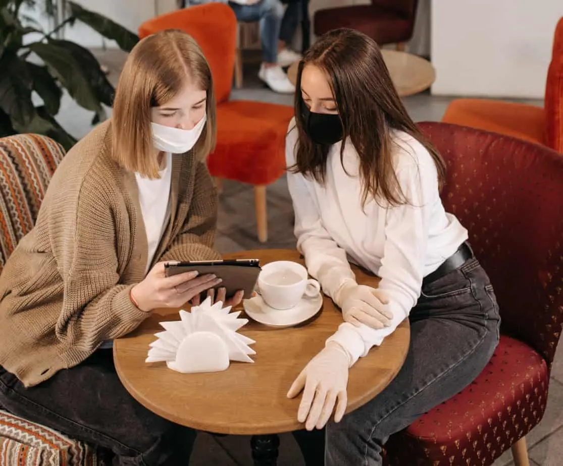 امرأتان تستمتعان بفوائد القهوة في المقهى أثناء ارتداء أقنعة الوجه.