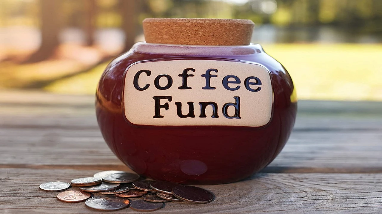 وعاء قهوة مملوء بالنقود على طاولة خشبية.
