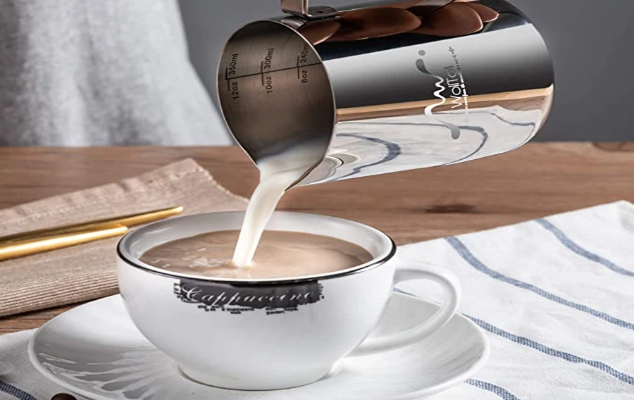 فنجان من القهوة يُسكب في فنجان باستخدام قدر بخار الحليب.